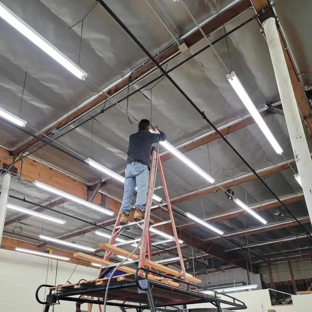 Mark Grippi on a ladder installing LED high-bay lighting in a commercial warehouse