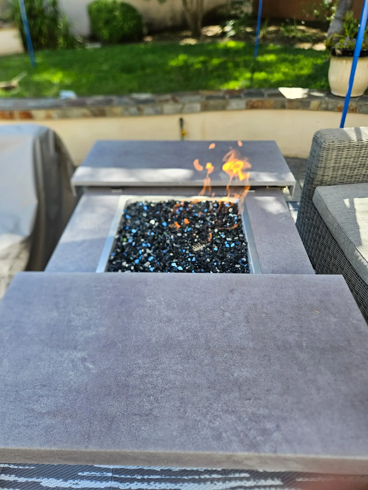 Outdoor fire feature with a stone surround and glass fire media, alight